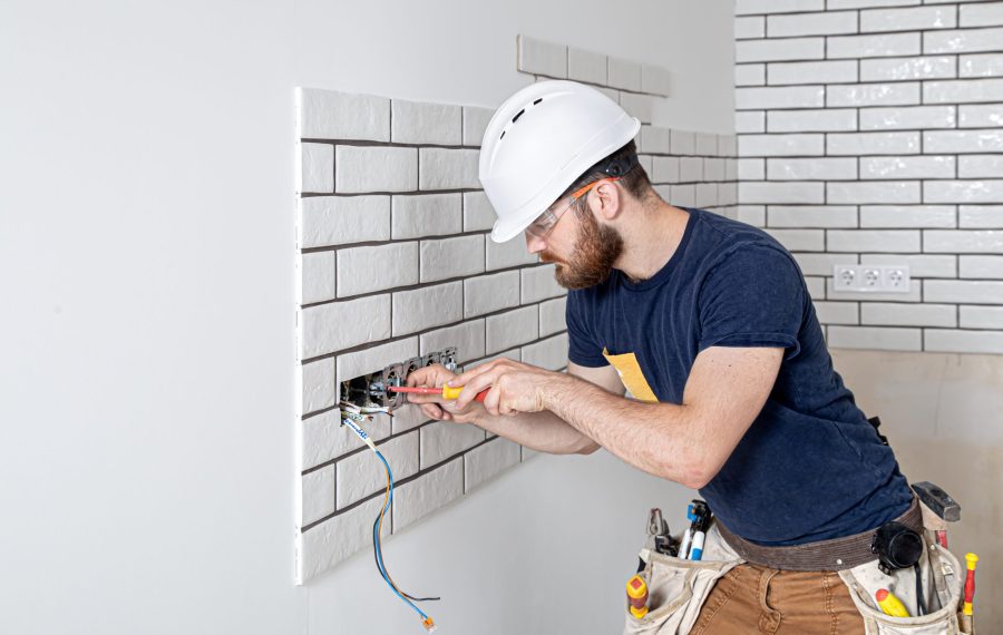 Electrician Builder at work, installation of sockets and switches. Professional in overalls with an electrician's tool. Against the background of the repair site. The concept of working as a professional.